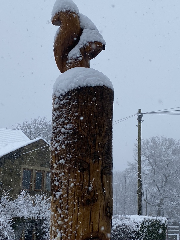 Wooden totem pole with wooden squirrel on the top covered in snow