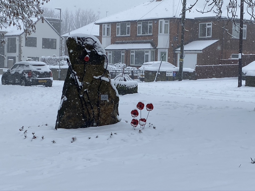 Stone war memorial with silhouette of a soldier surrounded with poppies and covered in snow