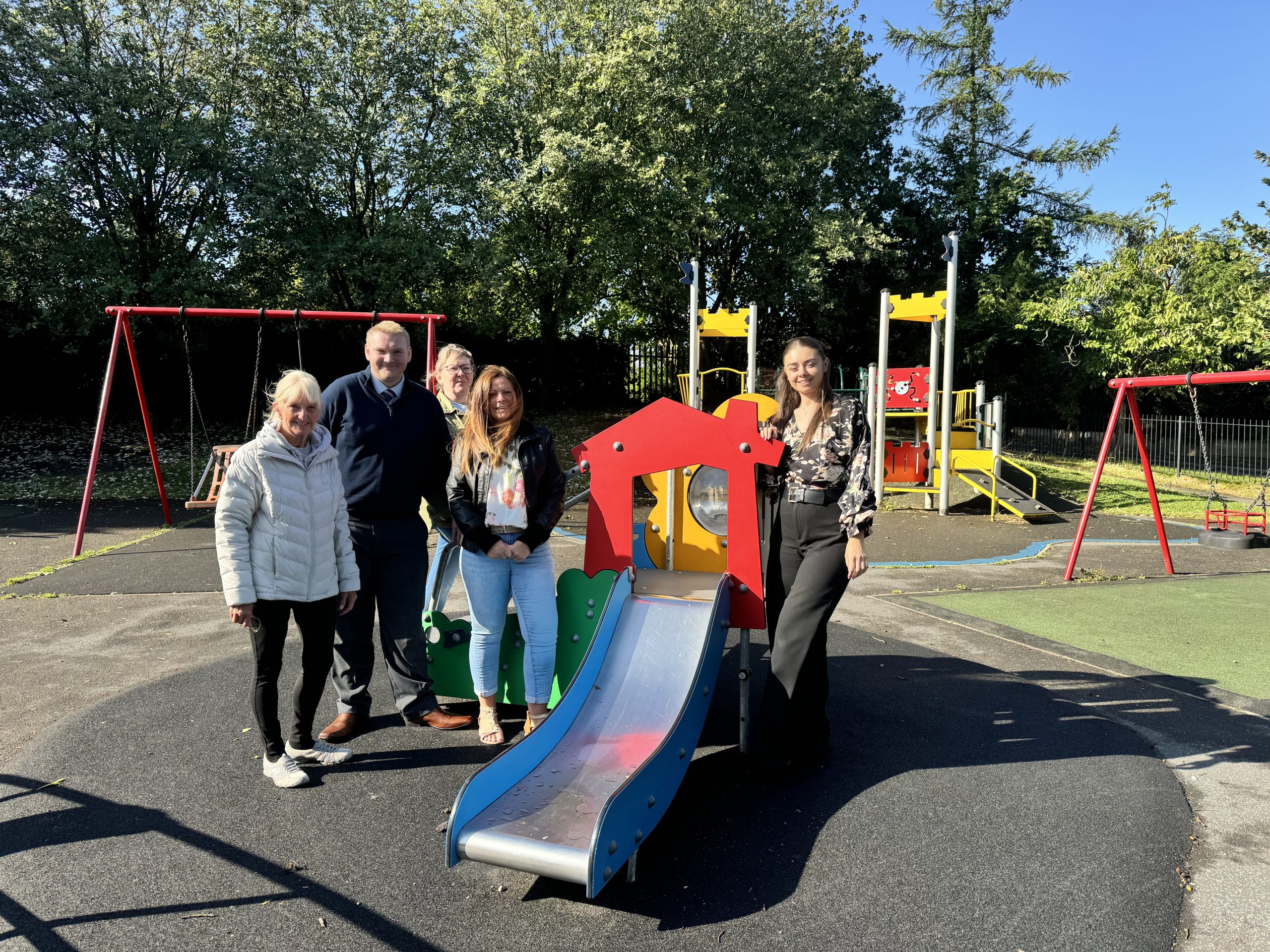 Gildersome Parish Councillor Amy May, with Parish Clerk Pat May, and Staff from Manning Stainton stood in playground next to a toddler's red and blue slide